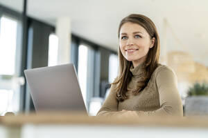 Businesswoman with brown hair looking away while standing in front of laptop at office - PESF02933