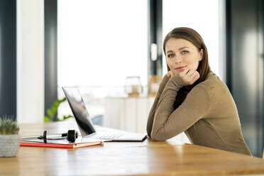 Businesswoman with hand on chin sitting at office - PESF02937