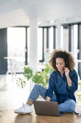 Eine Afro-Frau arbeitet im Kundenservice an einem Laptop und spricht über ein Headset in einer Büro-Cafeteria - PESF02941