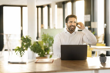 Smiling male professional looking away while talking through headset at office cafeteria - PESF02950