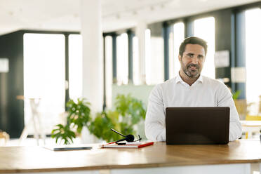 Male professional sitting in front of laptop at office cafeteria - PESF02954