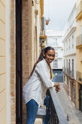 Lächelnde Frau, die sich auf einem Balkon an ein Geländer lehnt - JRVF00948