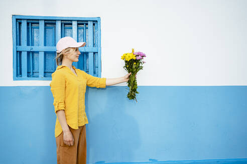 Junge Frau mit Mütze hält Blumen an der Wand - RCPF01171