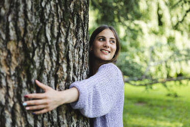 Glückliche Frau, die einen Baum in einem öffentlichen Park umarmt - MCVF00883