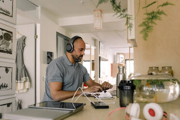 Businessman wearing headphones working on laptop while sitting at kitchen island - MASF23799