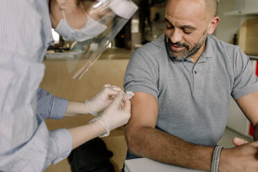 Mature man looking at female healthcare worker injecting medicine - MASF23812