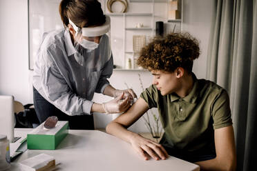 Female nurse giving COVID-19 vaccine to teenage boy at home - MASF23819