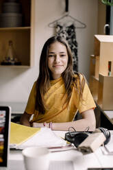 Porträt eines lächelnden Mädchens mit langen Haaren, das am Schreibtisch sitzt - MASF23840
