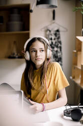 Mädchen mit Kopfhörern sitzt am Schreibtisch und schaut weg - MASF23847