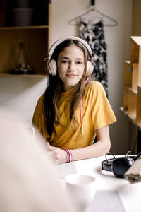 Porträt eines lächelnden Mädchens in einem gelben T-Shirt, das am Schreibtisch sitzt - MASF23848