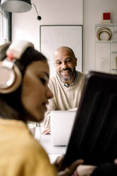 Lächelnder Vater, der seine Tochter ansieht, die ein digitales Tablet zu Hause zeigt - MASF23850