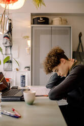 Tired boy reading book while studying at home - MASF23866