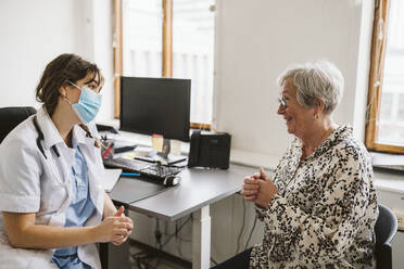 Lächelnde ältere Patientin im Gespräch mit einem medizinischen Experten mit Gesichtsmaske - MASF23909