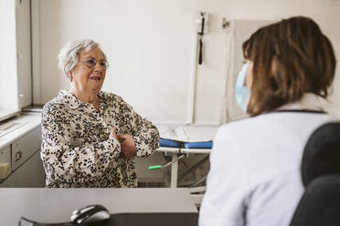 Senior female patient discussing with healthcare worker while consulting during COVID-19 - MASF23913