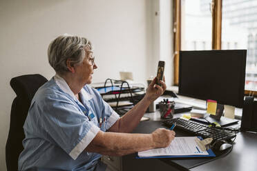 Ein älterer medizinischer Experte berät einen Patienten per Videoanruf, während er am Schreibtisch ein Rezept schreibt - MASF23915