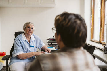 Eine ältere Ärztin berät einen männlichen Patienten in einer medizinischen Klinik - MASF23942