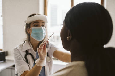Female doctor wearing protective mask and face shield doing patient's medical test - MASF23945