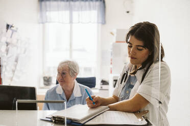Eine Mitarbeiterin im Gesundheitswesen schreibt ein Rezept, während sie neben einer älteren Krankenschwester steht - MASF23946