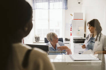 Ältere Krankenschwester im Gespräch mit einem Arzt, gesehen durch Glas in einer medizinischen Klinik - MASF23951