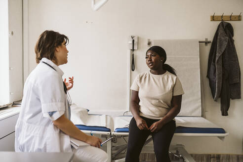 Weiblicher medizinischer Experte im Gespräch mit einem Patienten auf dem Untersuchungstisch in einer medizinischen Klinik - MASF23954