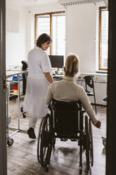 Smiling female medical expert looking at disabled woman visiting at medical clinic - MASF23968