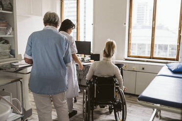 Rückansicht eines behinderten Patienten mit Ärztin und Krankenschwester in einer medizinischen Klinik - MASF23969