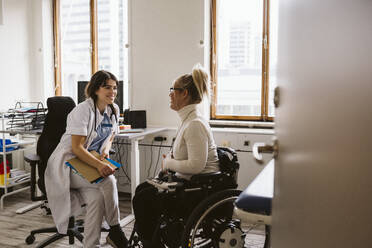 Lächelnder weiblicher medizinischer Experte, der eine behinderte Frau beim Gespräch in einer medizinischen Klinik beobachtet - MASF23979