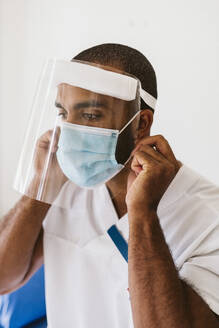 Männlicher Arzt mit Gesichtsschutzmaske und Gesichtsschutzschild während COVID-19 - MASF23983