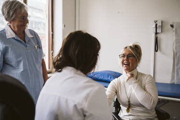 Ältere Krankenschwester betrachtet eine behinderte Frau, die sich mit einem Arzt in einer medizinischen Klinik berät - MASF23984