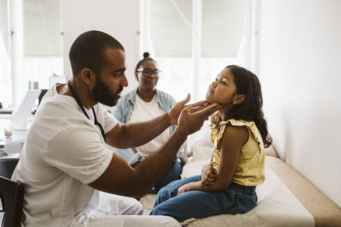 Männlicher Arzt, der den Hals eines Mädchens untersucht, während er in einer medizinischen Klinik sitzt - MASF24020