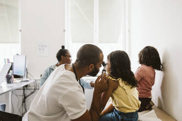 Männlicher Kinderarzt schaut durch ein Otoskop, während er das Ohr eines Mädchens in einer medizinischen Klinik untersucht - MASF24021