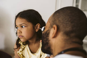 Male healthcare worker examining girl's ear at medical clinic - MASF24025