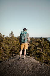 Reifer Mann in voller Länge mit Rucksack auf einem Felsen stehend an einem sonnigen Tag - MASF24044