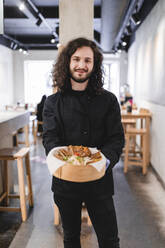 Portrait of male chef with dumplings in bowl standing at restaurant - MASF24096