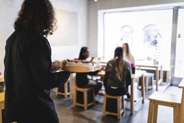 Rückansicht eines männlichen Kellners, der weiblichen Kunden im Restaurant Essen serviert - MASF24099