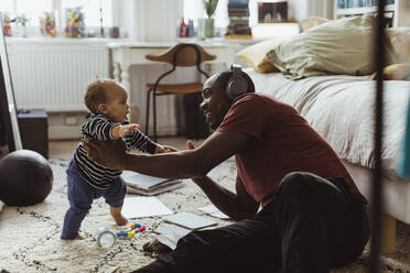 Vater hält männliches Kleinkind, während er im Schlafzimmer zu Hause sitzt - MASF24165