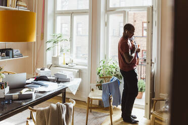 Businessman carrying baby boy while standing by door at home office - MASF24166