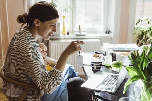 Geschäftsfrau zeigt Etikett auf Videoanruf durch Laptop im Heimbüro - MASF24185
