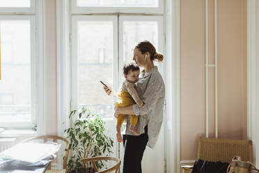 Geschäftsfrau mit Baby und Smartphone in der Hand zu Hause - MASF24213