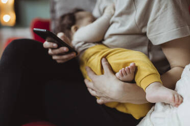 Midsection von Mutter mit Baby Junge mit Smartphone im Wohnzimmer - MASF24218