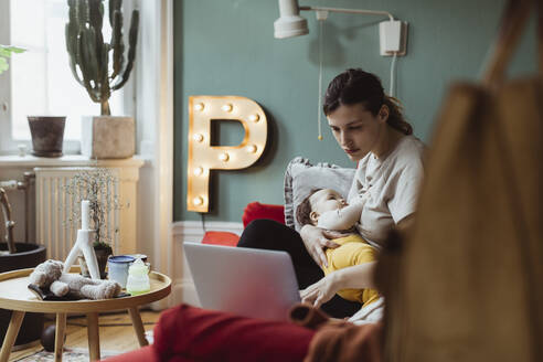 Berufstätige Frau arbeitet am Laptop, während sie sich zu Hause um ihren kleinen Sohn kümmert - MASF24220