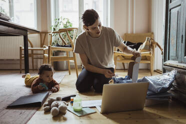 Eine Unternehmerin packt ein Hemd in eine Schachtel, die ihr kleiner Sohn zu Hause aufbewahrt - MASF24221