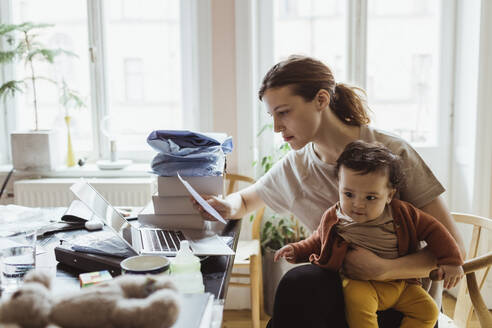 Geschäftsfrau liest ein Dokument, während sie mit einem kleinen Jungen im Wohnzimmer sitzt - MASF24225