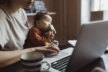 Unternehmerin mit kleinem Jungen arbeitet am Laptop im Büro zu Hause - MASF24239