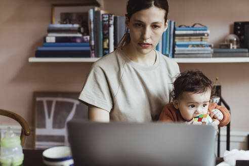 Geschäftsfrau, die einen Laptop benutzt, während sie mit einem kleinen Jungen zu Hause sitzt - MASF24241