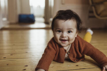 Portrait of smiling male toddler lying on floor at home - MASF24245