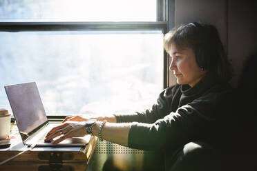 Geschäftsfrau, die einen Laptop benutzt, während sie im Zug am Fenster sitzt - MASF24254