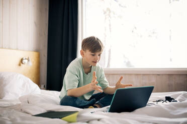 Boy attending video call while gesturing during homeschooling in bedroom - MASF24274