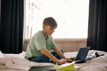 Junge mit Laptop bei den Hausaufgaben im Schlafzimmer - MASF24278