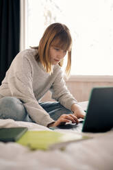 Teenager-Mädchen tippt auf einem Laptop, während sie zu Hause Hausaufgaben macht - MASF24280